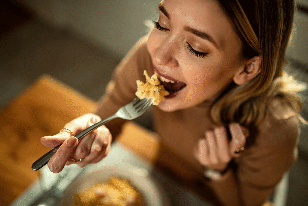 Woman happily eating mac and cheese with her eyes closed.