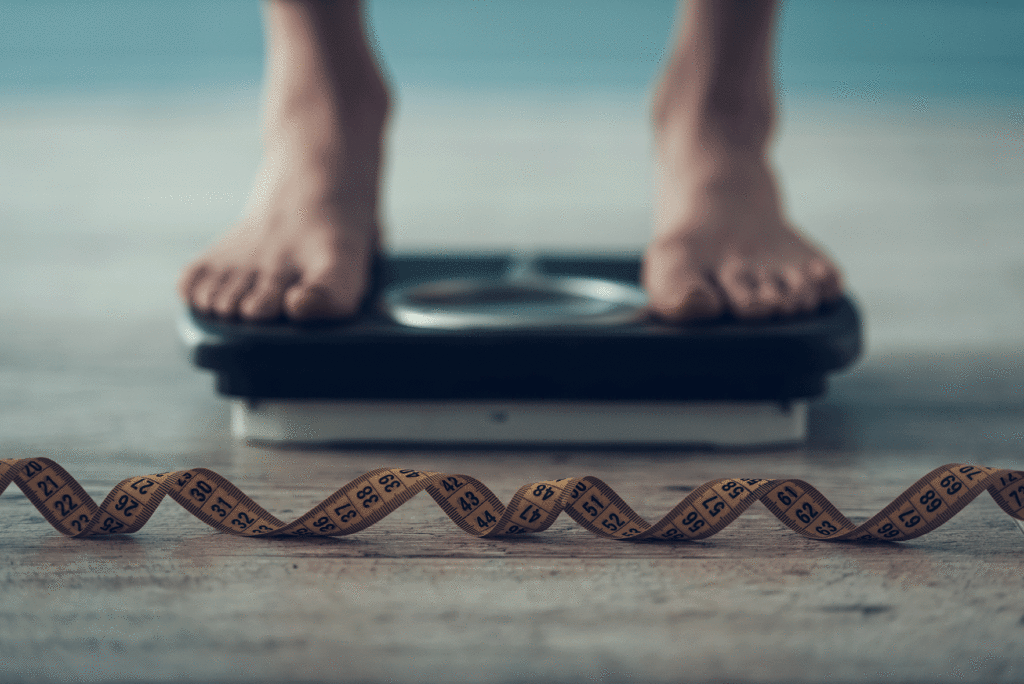 Feet standing on a scale with measuring tape in the foreground