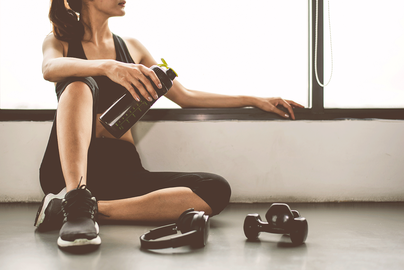 Woman resting near a window with dumb bells by her feet